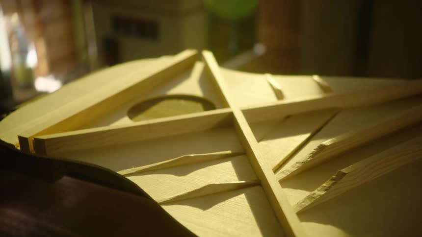 A slow pull-back reveals the intricate interior bracing of an acoustic guitar being built in a luthier's workshop