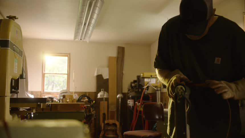 A man carefully works with a belt sander in a sun-drenched workshop