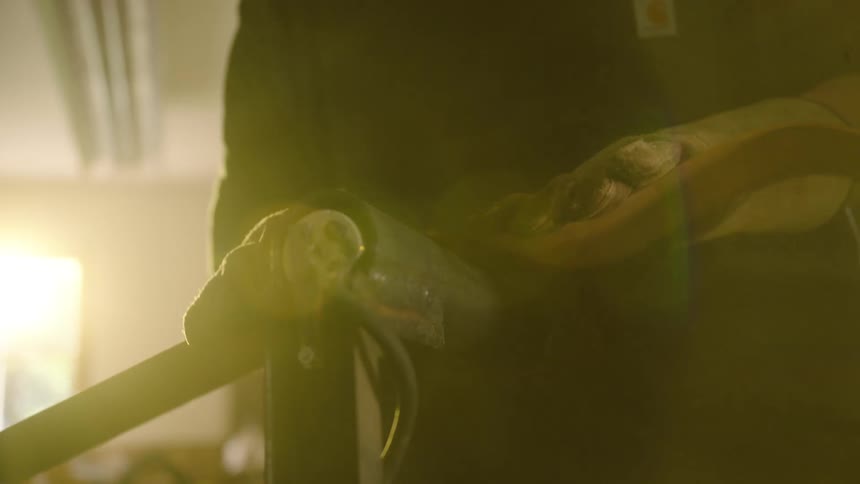 A craftsman with gloved hands meticulously shapes a leather strap on a machine in a sun-drenched workshop