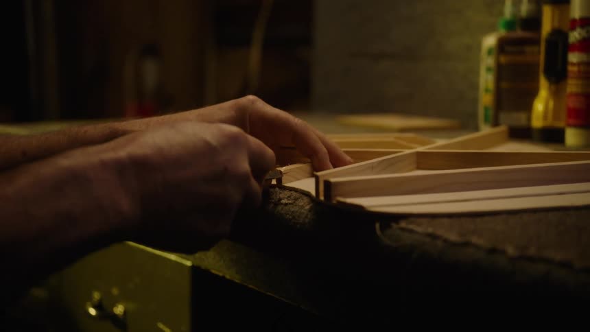 A skilled craftsman meticulously fits a small wooden brace into a delicate frame inside a dimly lit workshop