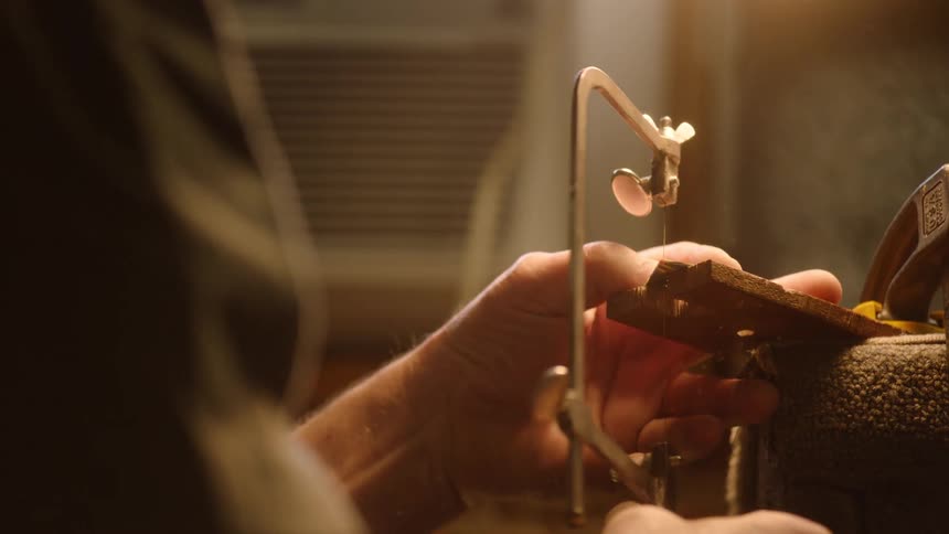 A skilled woodworker meticulously uses a fine coping saw to cut a piece of wood held in a workshop vise in slow motion
