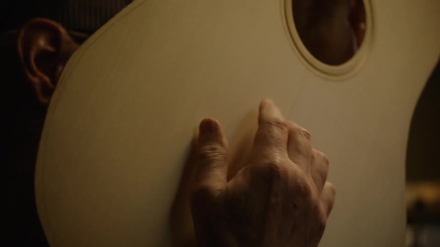A skilled luthier carefully inspects the soundboard of a handcrafted acoustic guitar in a dimly lit workshop