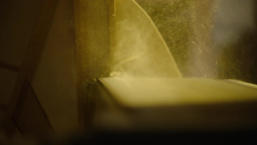 An artisan woodworker carefully uses a belt sander to shape a piece of wood, sending a cloud of sawdust into the air in slow motion