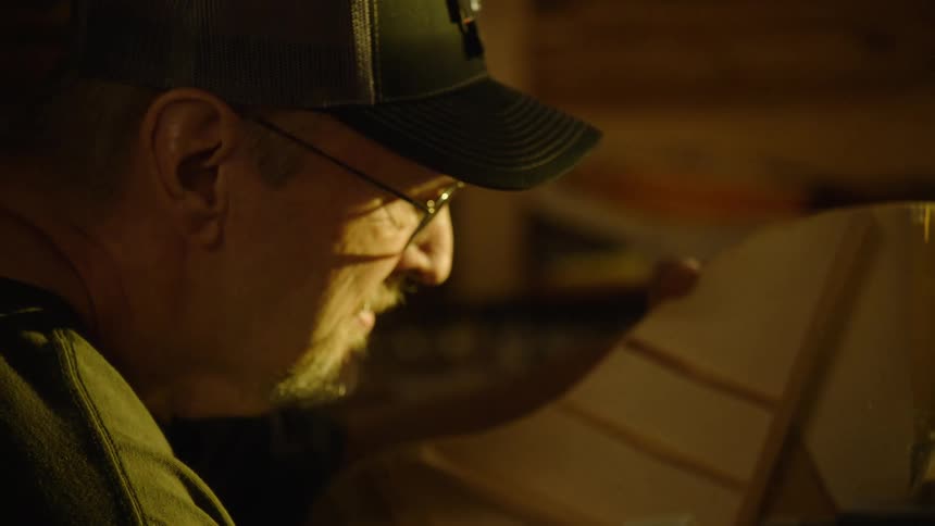 A luthier carefully sands the wooden body of a custom guitar in his workshop, with sawdust catching the warm light in slow motion