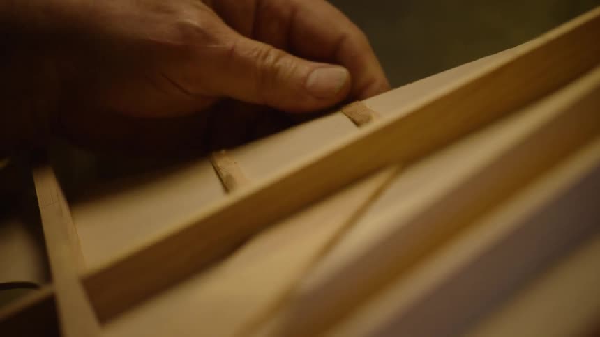 A skilled luthier carefully places wooden braces inside the body of a handmade acoustic guitar