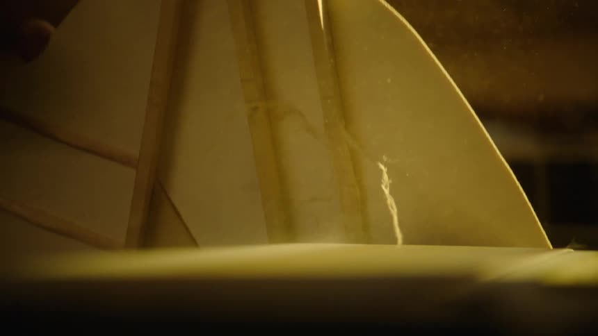 Sawdust flies in slow motion as a craftsman carefully sands the wooden body of a guitar in his workshop