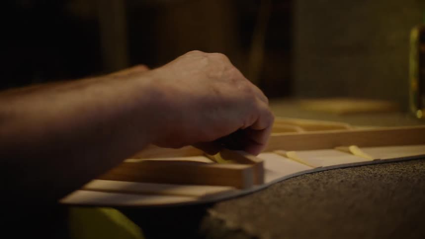 A skilled luthier carefully assembles the intricate wooden bracing on the soundboard of a guitar in their workshop