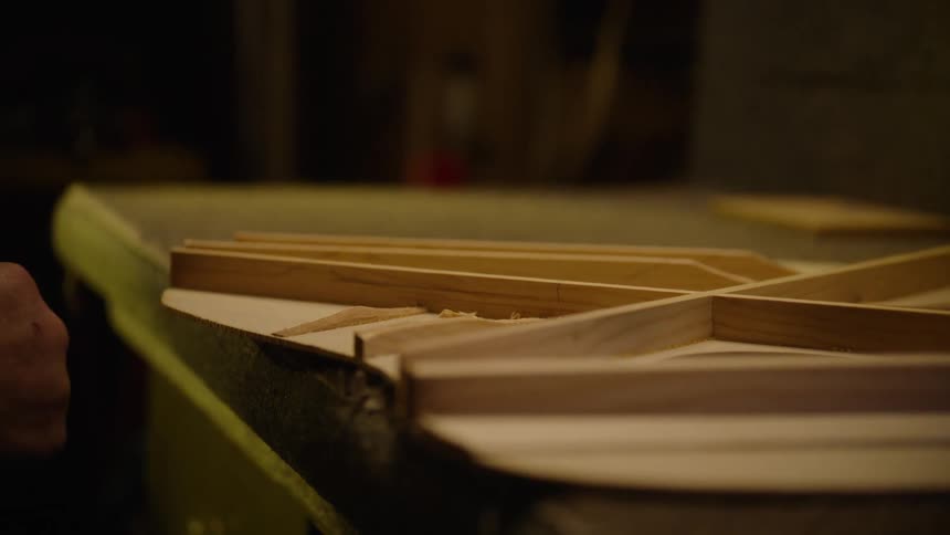 A skilled luthier carefully carves and cleans the internal wooden bracing of a handmade acoustic guitar in their workshop