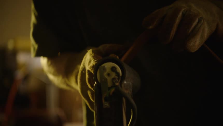 A pair of gloved hands work on the wiring of a machine in a dimly lit workshop