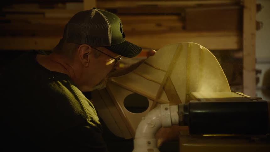 In a warmly lit workshop, a skilled luthier meticulously sands the body of a handmade acoustic guitar in slow motion