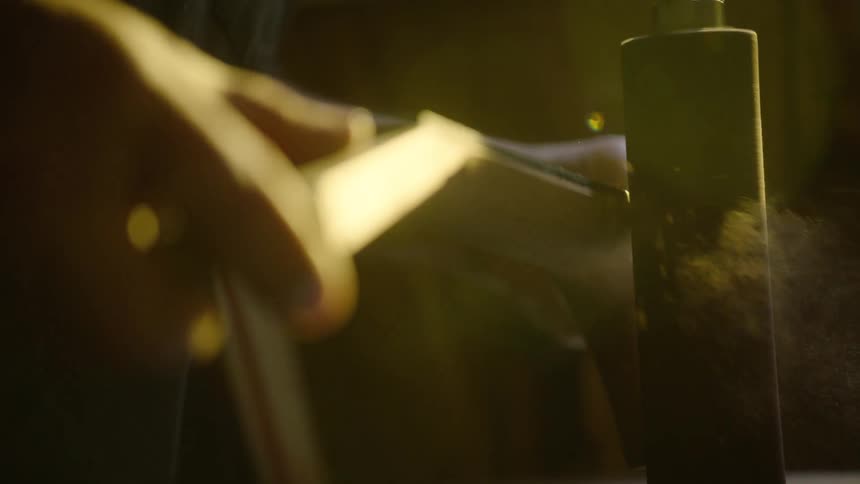 Close up slow motion shot of a craftsman sanding a piece of wood, with sawdust particles suspended in a warm light