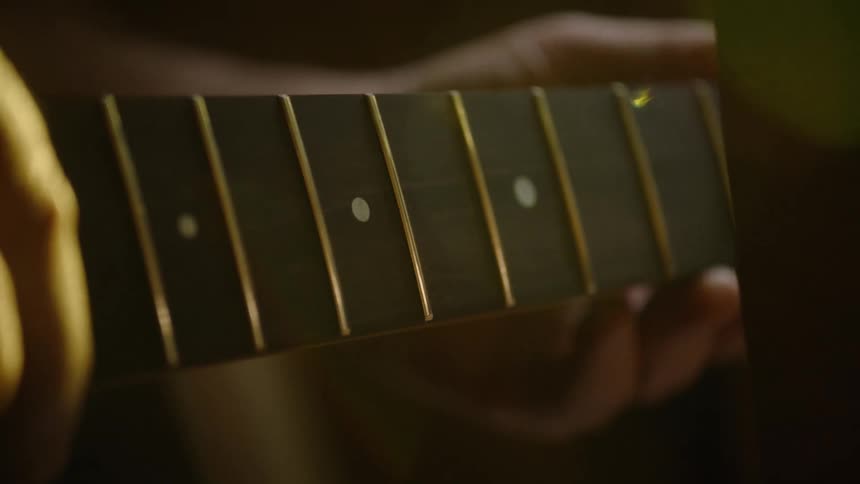 A luthier meticulously sands and shapes the wooden neck of a guitar in a warmly lit workshop, with dust particles dancing in the light