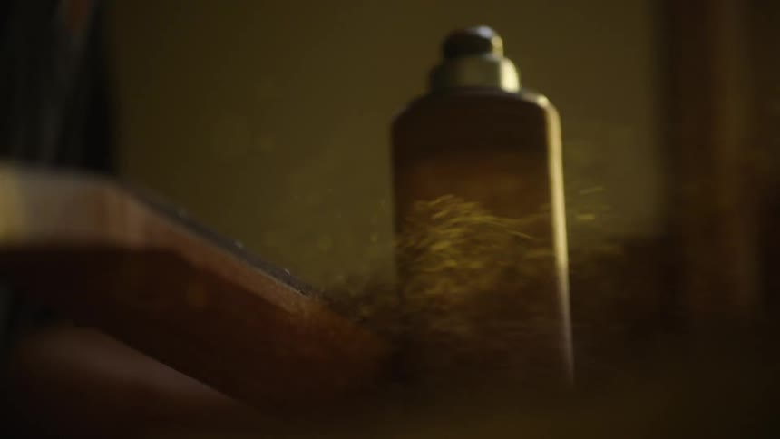 Sawdust flies through the air in a warm, dusty workshop as a craftsman sands a piece of wood in extreme slow motion