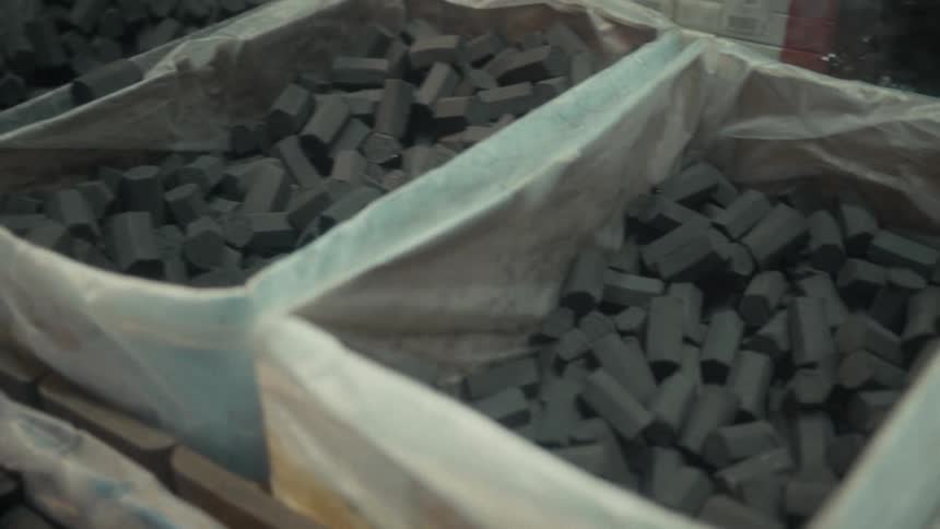 A slow pan reveals large bags filled with hexagonal charcoal briquettes at an indoor market