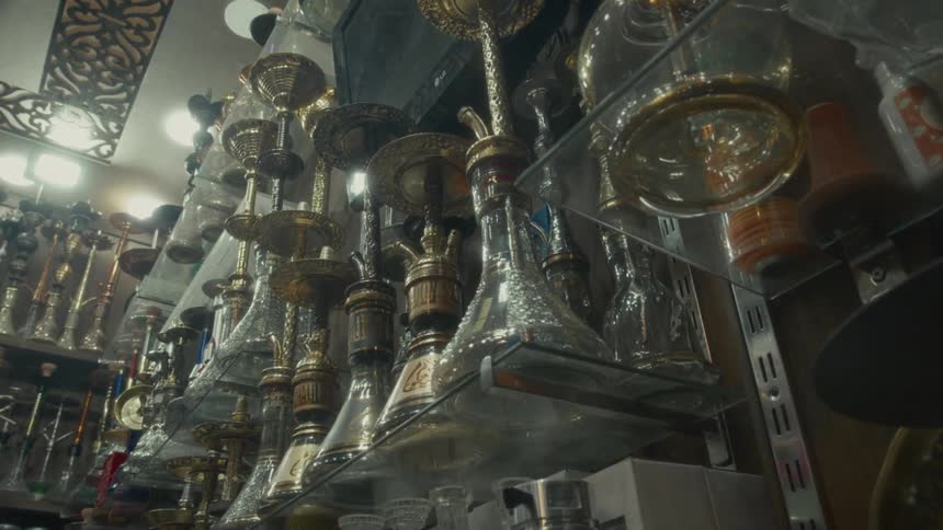 A low-angle view of various ornate hookahs displayed on glass shelves in a traditional shop