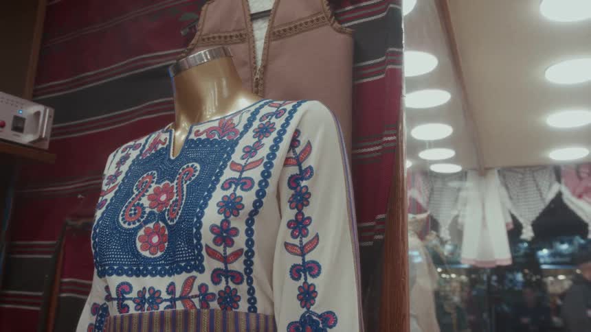 A traditional embroidered dress is displayed on a mannequin in a vibrant market shop window at night