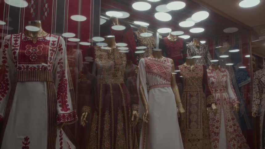 Mannequins adorned with traditional embroidered dresses are displayed in a brightly lit storefront window