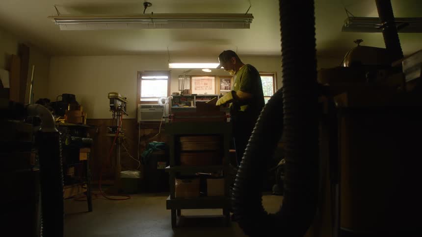 A craftsman works diligently on a woodworking project in his dimly lit, rustic workshop before walking away