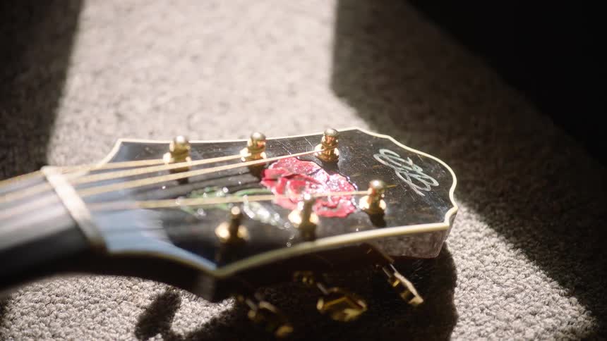 A slow focus pull along the headstock of an acoustic guitar with a beautiful rose inlay, bathed in a dramatic sunbeam