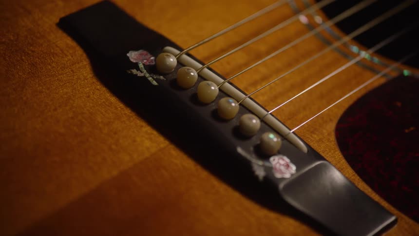 A detailed close-up shot slowly pans across the intricate rose inlay on the bridge of a wooden acoustic guitar