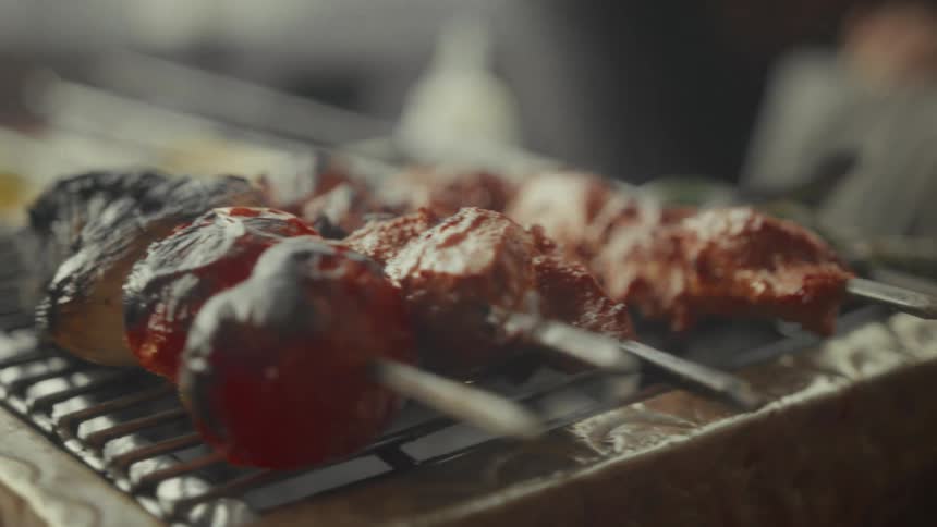 A close-up slow-motion shot of savory meat and vegetable kebabs smoking and charring on a hot grill