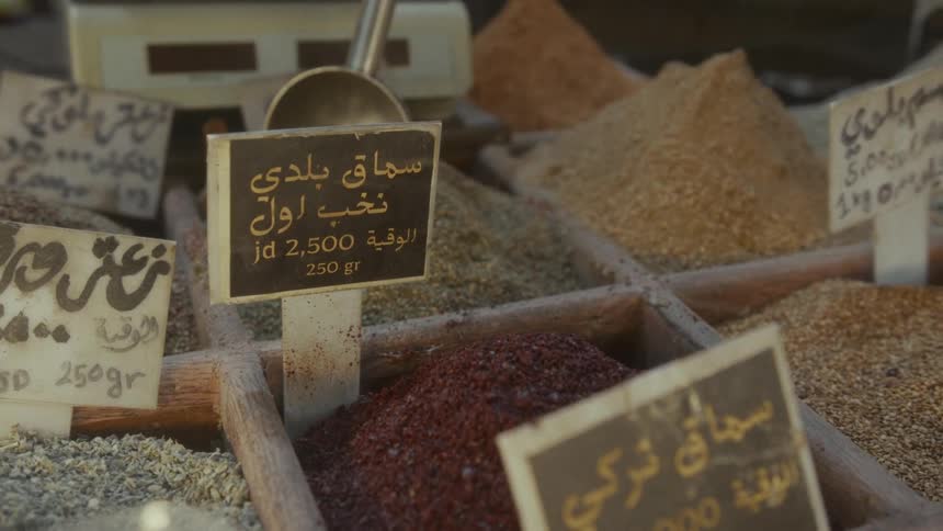 A close-up of colorful spices with Arabic price tags displayed in wooden bins at a traditional market