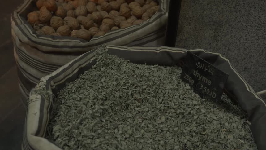 A close-up view of a burlap sack filled with dried thyme for sale at an indoor market
