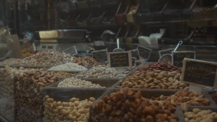 An assortment of fresh nuts displayed in bins with Arabic price tags at a local market stall