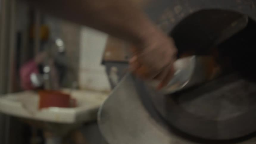 Slow-motion close-up of a worker pouring seasoned pumpkin seeds from a scoop into a rotating industrial roaster