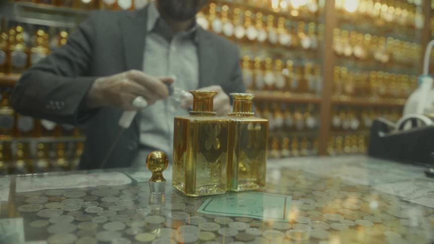 A skilled perfumer in a traditional Middle Eastern souk meticulously handles ornate gold perfume bottles on a unique coin-covered counter