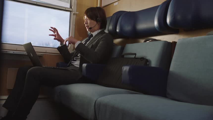 Slow reveal of a businessman working remotely, engaged in a video call on his laptop inside a moving train