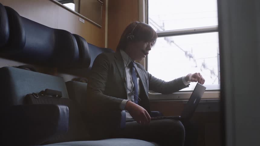 A young businessman conducts an online meeting on his laptop with a headset while traveling in a train compartment