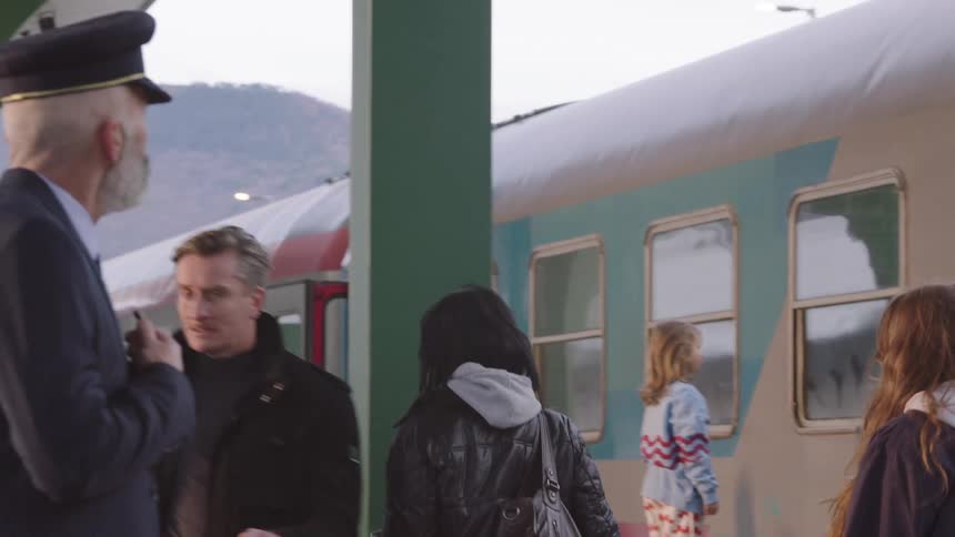 Passengers walk along a bustling train station platform as a conductor observes the scene