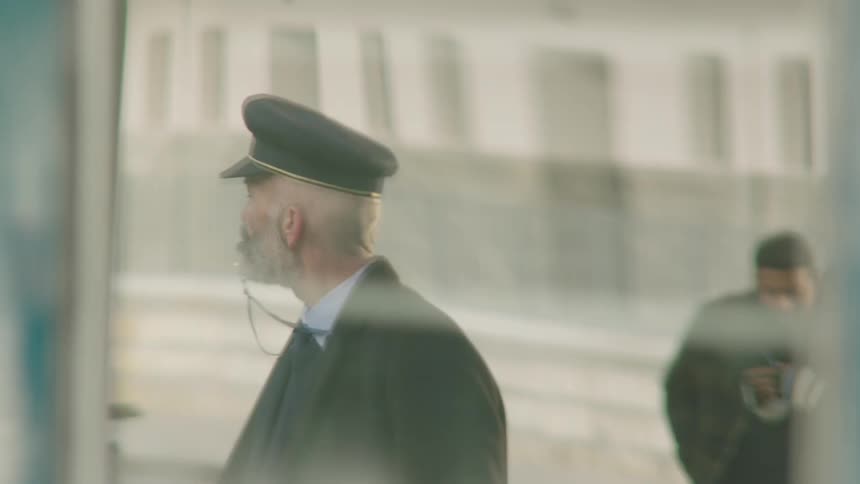 Slow motion shot of a vintage train conductor blowing his whistle on a hazy station platform