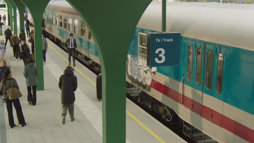 High-angle view of travelers with luggage walking along a busy platform and boarding a train at Track 3