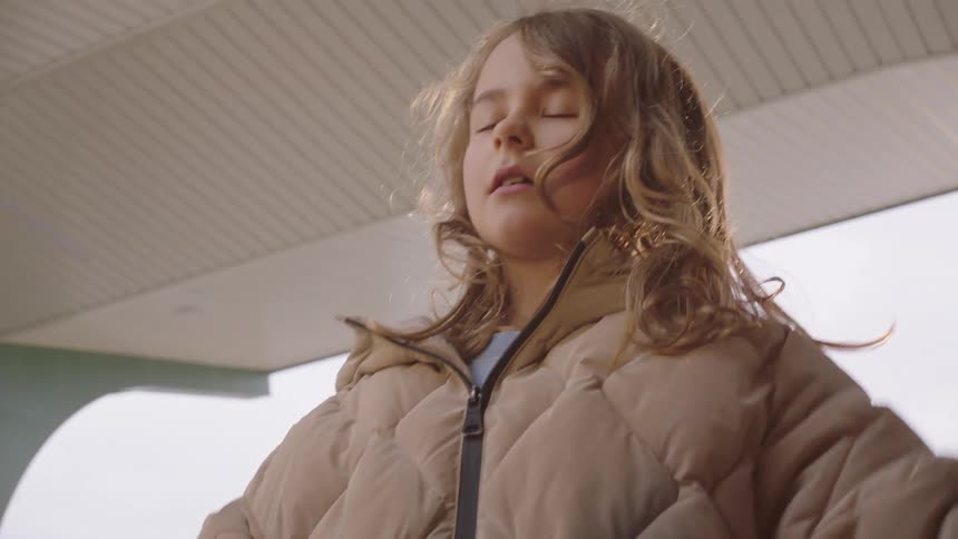 Slow-motion close-up of a young girl in a puffer jacket looking up with a worried and curious expression