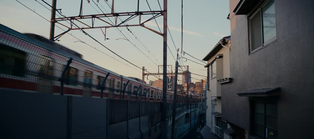 A commuter train travels through a quiet urban neighborhood in Japan as the golden hour sun sets