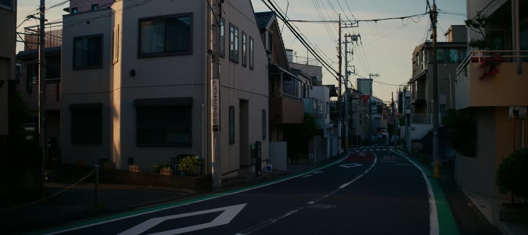 A lone man walks down a quiet residential street in a Japanese city during the golden hour