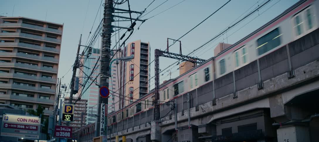 A commuter train travels along an elevated railway through a dense urban landscape in Japan at dusk