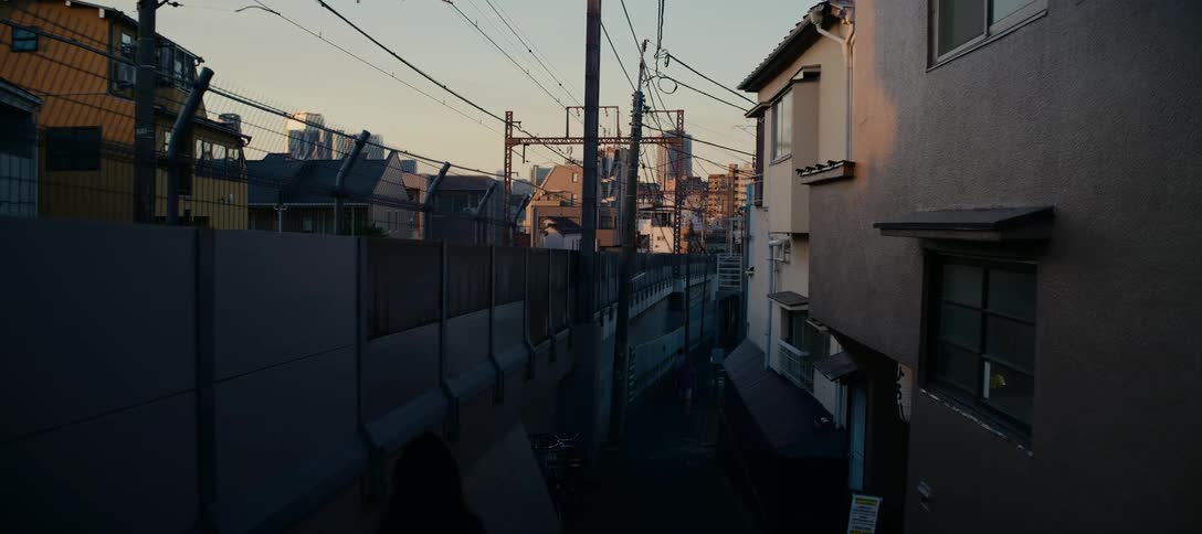 Pedestrians walk through a quiet, narrow urban alley in Tokyo during a warm golden hour sunset