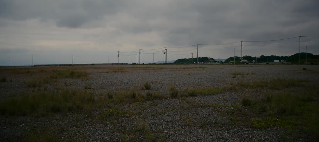 A wide, static shot of an empty, desolate gravel lot under a dark, overcast sky