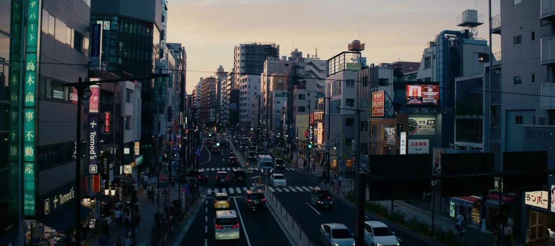 A wide shot shows busy city traffic and pedestrians on the streets of Tokyo, Japan during a beautiful sunset