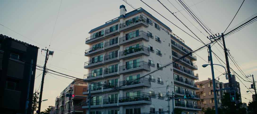 A low-angle shot of a multi-story apartment building on a quiet city street in Japan at dusk
