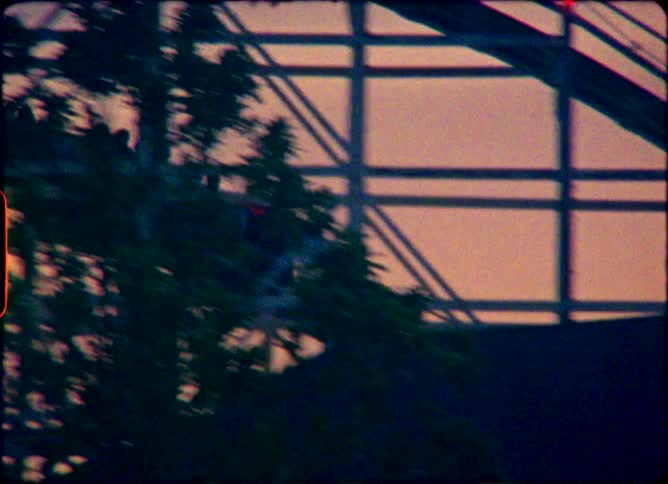 Silhouetted figures enjoy a ride on a classic wooden roller coaster against a beautiful sunset in this vintage film clip