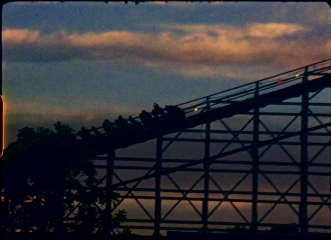 A silhouetted roller coaster climbs a hill against a beautiful sunset sky in this authentic vintage 8mm film clip