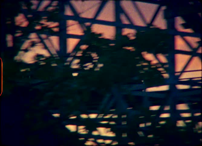 Vintage 8mm footage captures the silhouette of a wooden roller coaster as it speeds along the tracks against a stunning sunset sky
