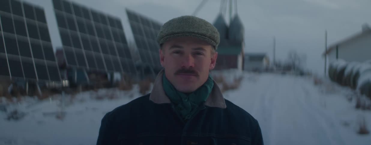 Portrait of a serious farmer with a mustache standing in front of solar panels on his snowy farm at dusk