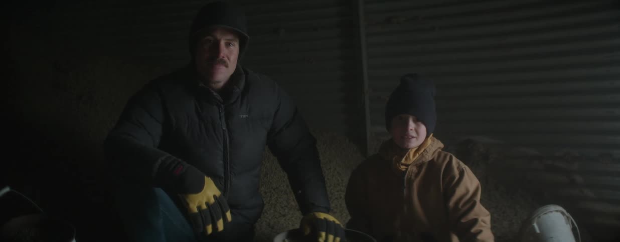 A proud farmer and his young son sit together in a dimly lit grain silo on their farm
