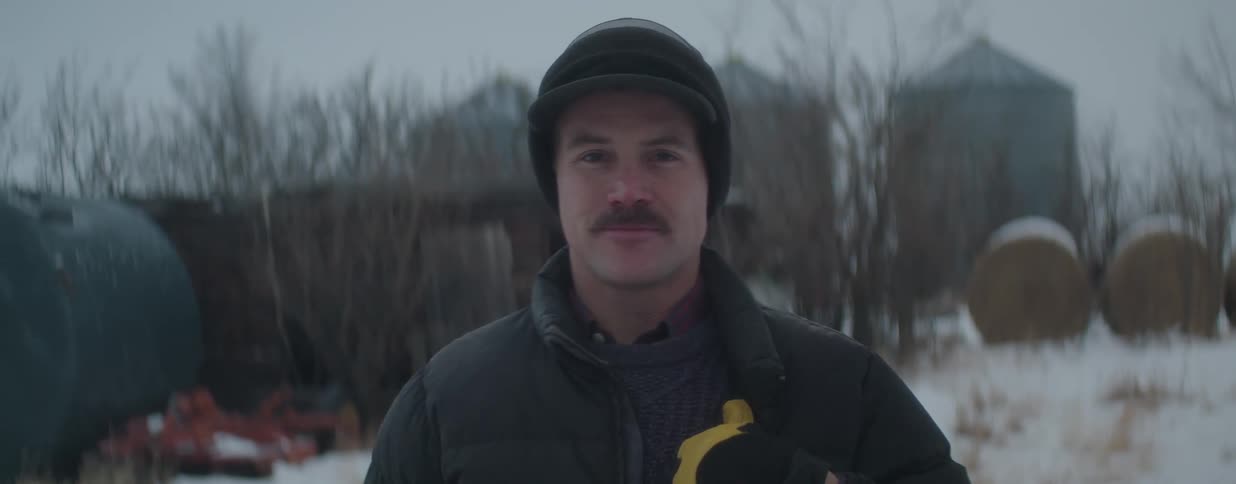Portrait of a mustached farmer wearing winter clothing and looking at the camera on a snowy day at the farm