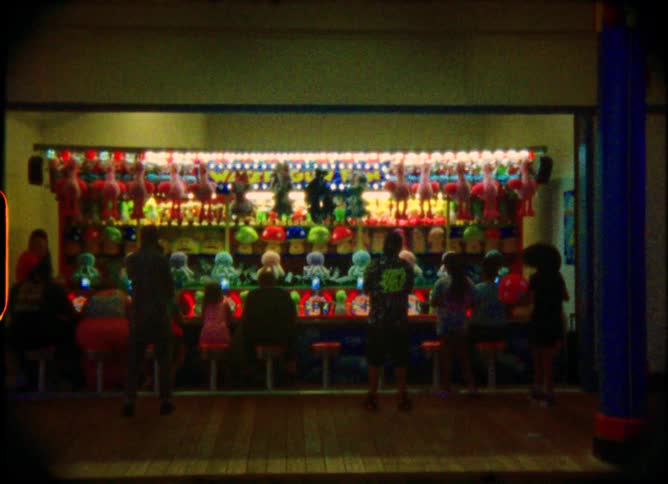 Vintage Super 8 film captures the nostalgic glow of people playing a brightly lit carnival game at night